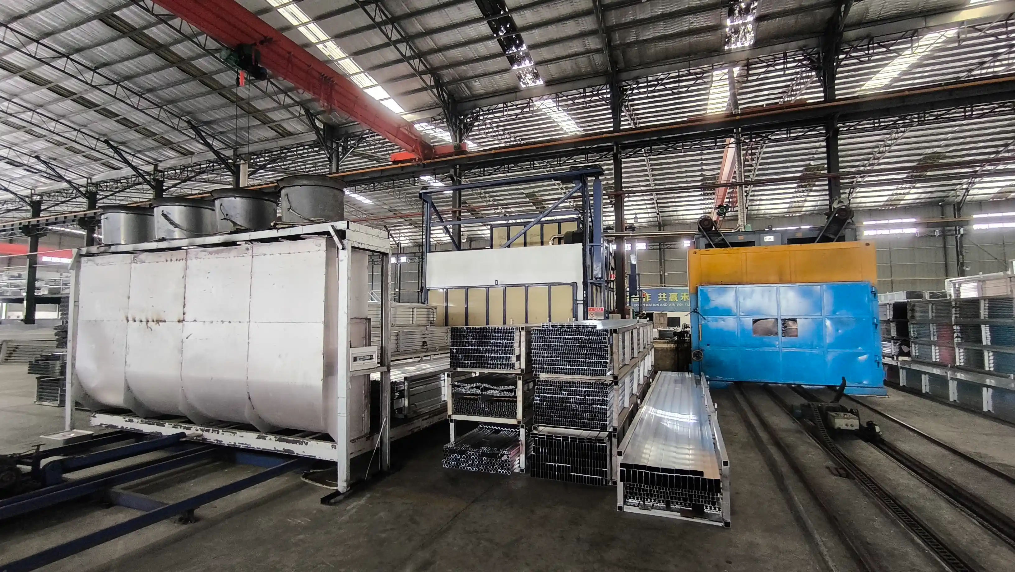 Industrial aging furnace oven and racks of stacked aluminum extrusion profiles on rail carts in the heat treatment workshop