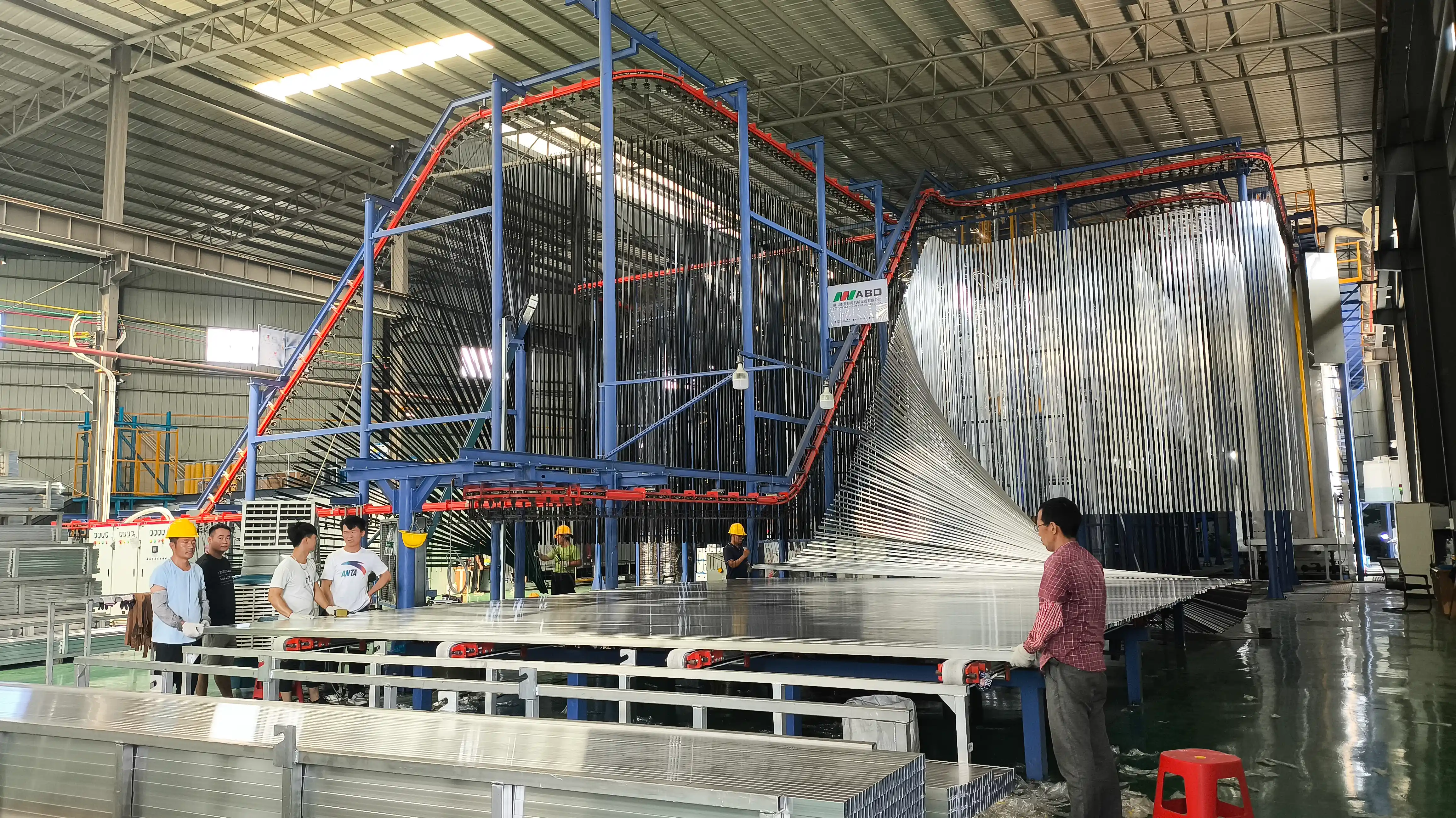 Automated vertical powder coating line with hanging aluminum extrusion profiles and workers in the surface treatment workshop