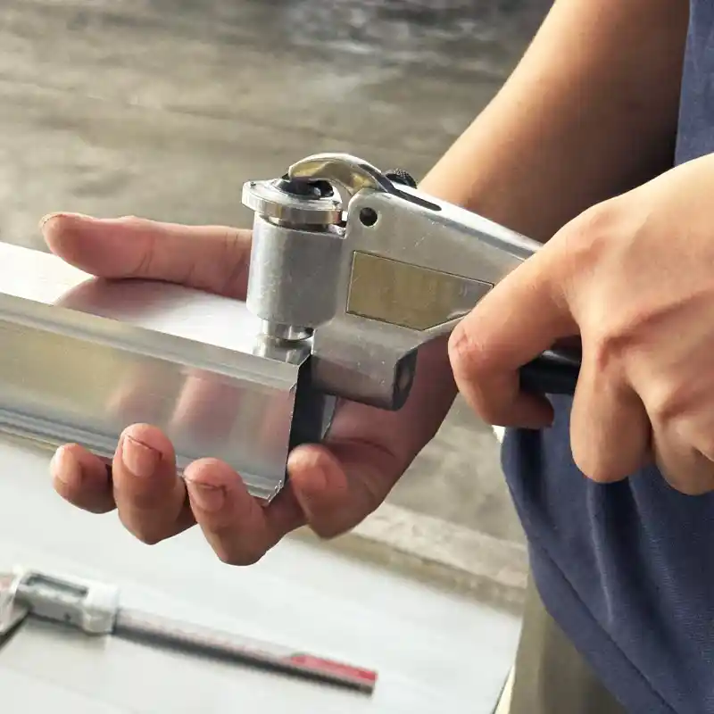 Quality control technician using a Webster hardness tester on an extruded aluminum profile, with a digital caliper nearby for thickness measurements.