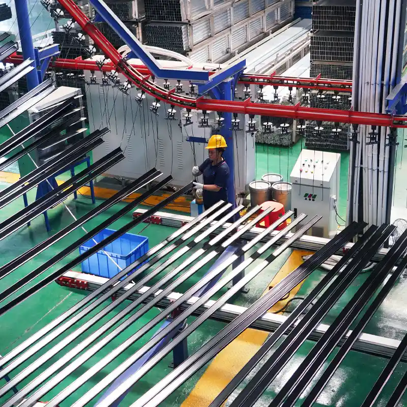 Black aluminum profiles moving along an overhead conveyor system during the powder coating process.