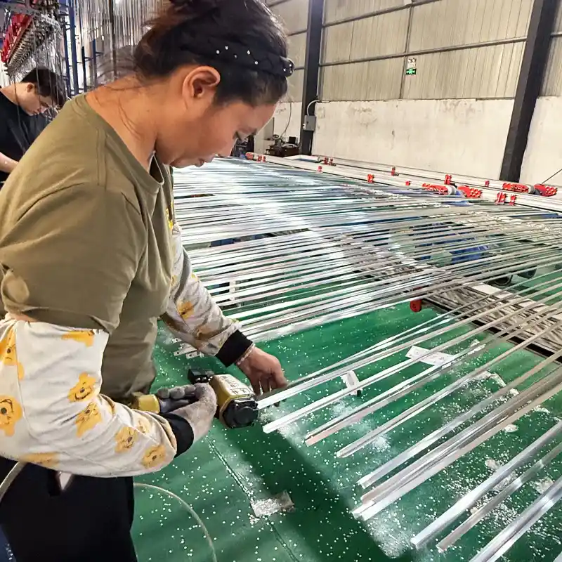 Female factory worker using a pneumatic tool to drill and process slender aluminum profiles on a green workbench.