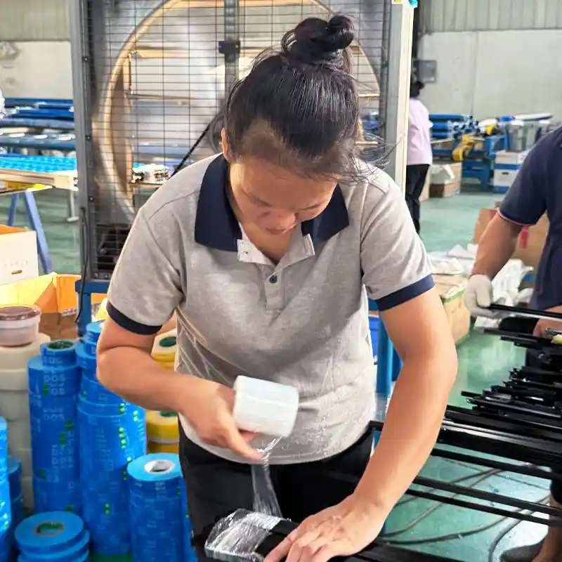 Factory worker applying stretch wrap film to bundle black aluminum profiles for safe shipping.