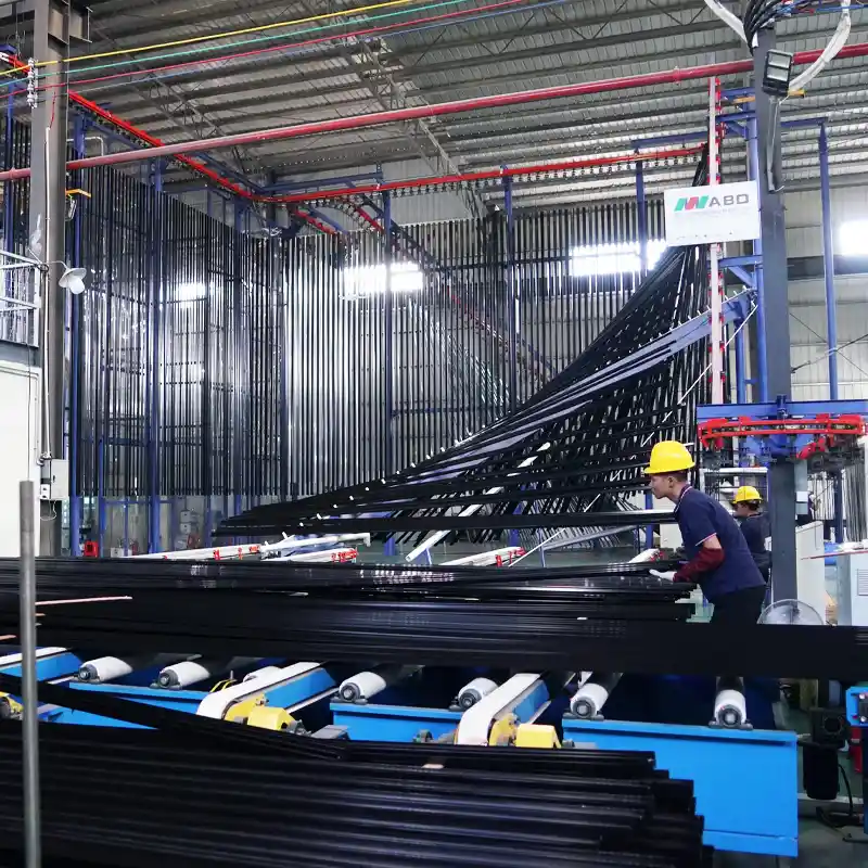 Worker loading black aluminum profiles onto an automated overhead conveyor system for further processing.