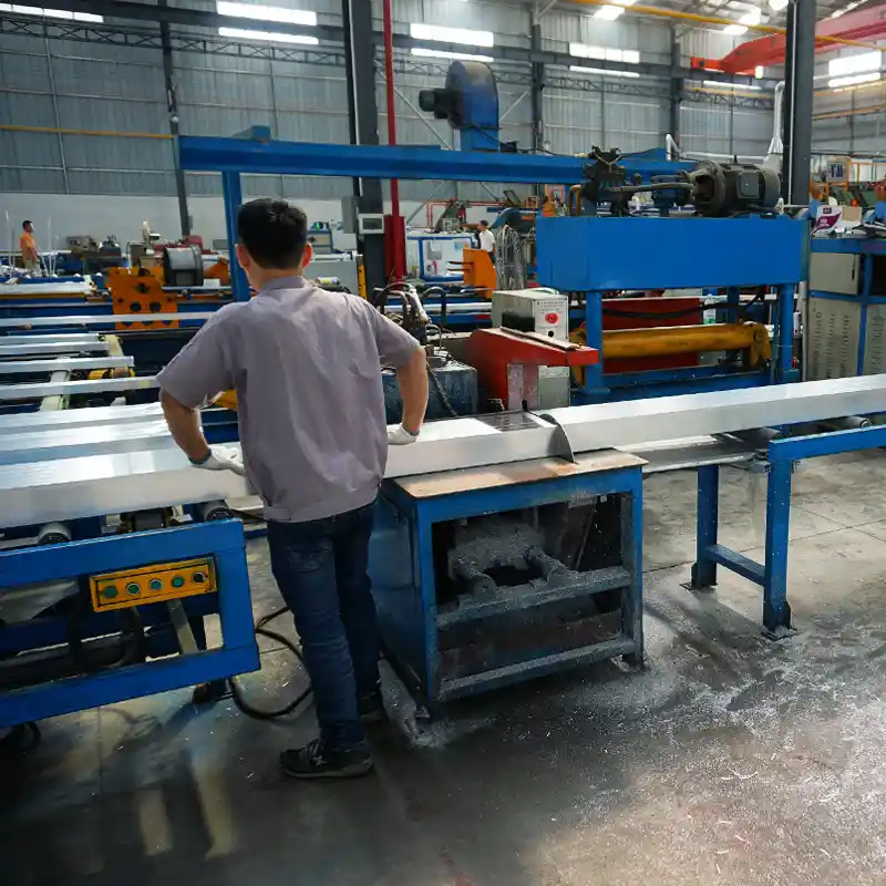 Operator working at an automated aluminum cutting and traction machine processing wide architectural profiles.