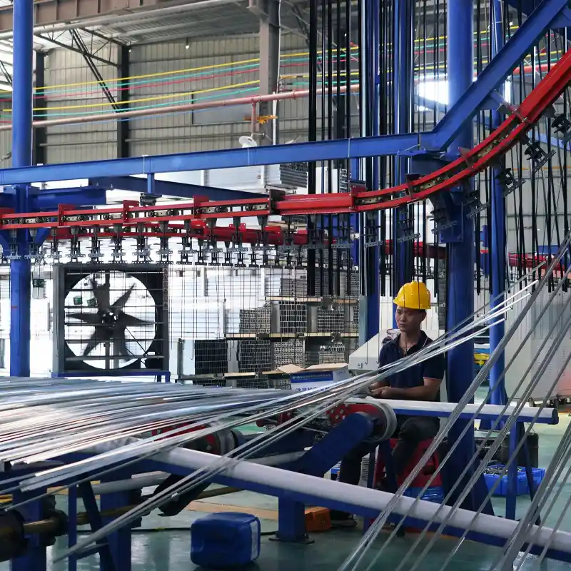 Worker loading slender aluminum extrusions onto a heavy-duty overhead conveyor system for automated surface treatment.