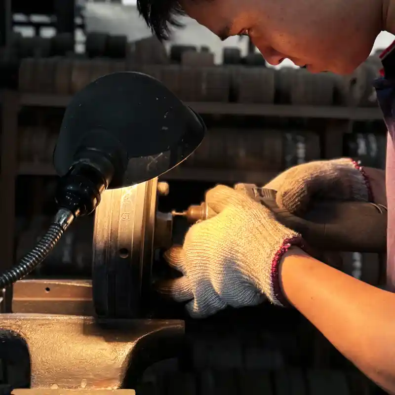 Skilled worker using a rotary tool for precision grinding of an aluminum extrusion die under focused lighting.