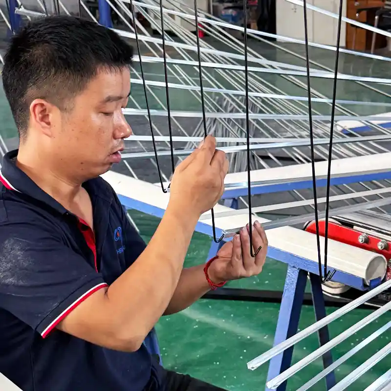 Factory worker carefully hanging slim aluminum profiles onto wire fixtures for surface treatment.