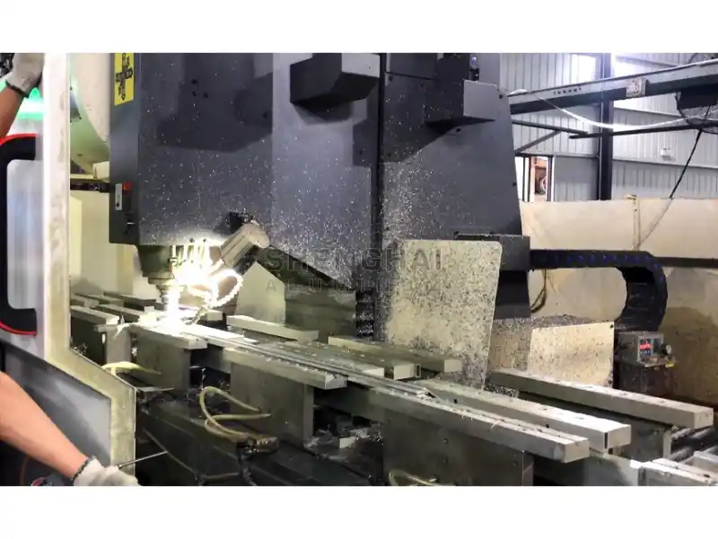 Industrial-grade multi-axis CNC machining center in operation, precision cutting an aluminum profile in a factory environment.